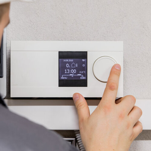 A person adjusting a modern digital HVAC thermostat, setting the temperature for efficient heating and cooling control. The image highlights the importance of proper thermostat use for maintaining a comfortable indoor environment.