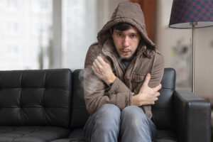 man in coat shivering from cold in his living